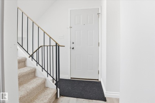 Entryway featuring a panel door, light-toned wood-finish flooring, and a carpeted staircase with a metal railing - 857 Erin Place, Edmonton, AB 