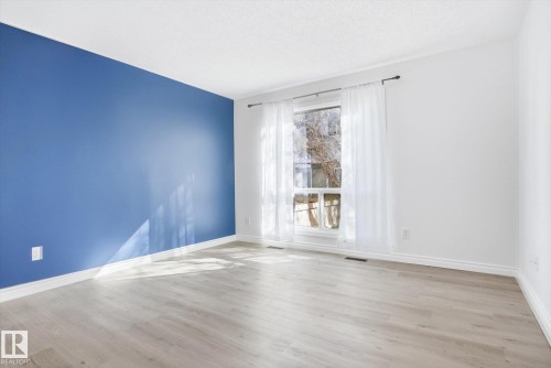 Spacious room featuring light wood-finish flooring, a prominent blue accent wall, and white trim - 857 Erin Place, Edmonton, AB 