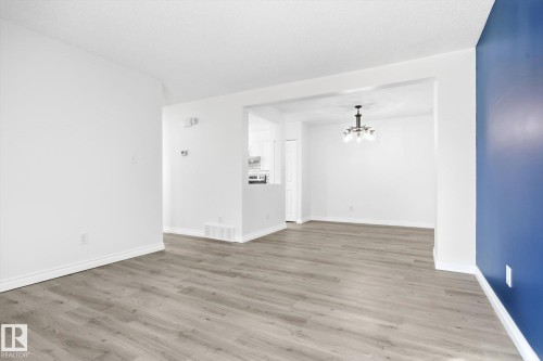 Open-concept interior featuring wood-finish flooring, white baseboards, and a contemporary chandelier - 857 Erin Place, Edmonton, AB 