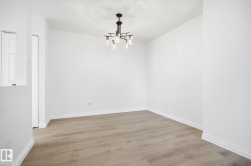 Open room featuring wood-finish flooring, white baseboards, a modern chandelier with exposed bulbs, and a white paneled door - 857 Erin Place, Edmonton, AB 