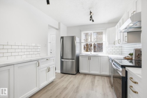Bright kitchen featuring stainless steel appliances, white cabinetry with gold-tone hardware, white subway tile backsplash, and wood-finish flooring - 857 Erin Place, Edmonton, AB 