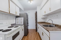 Galley kitchen featuring white cabinetry with gold-tone hardware, wood-finish flooring, white tile backsplash, a stainless steel refrigerator, and a stainless steel sink with a chrome faucet - 