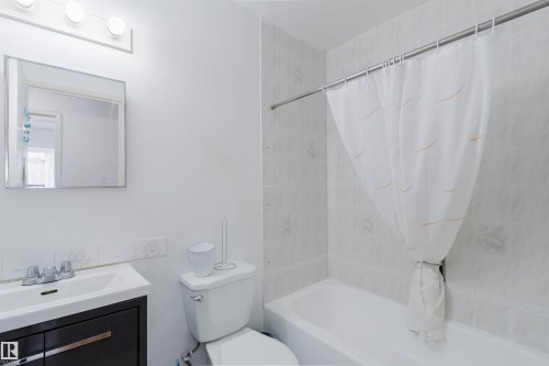Bathroom featuring a white bathtub, tiled shower surround, and a dark wood-finish vanity with an integrated sink - 4 14310 80 Street, Edmonton, AB 