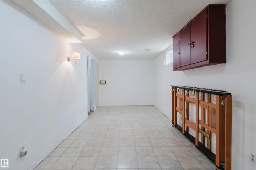 Spacious room featuring light-toned tiled flooring, white painted walls, and a textured ceiling - 4 14310 80 Street, Edmonton, AB 