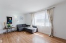 Spacious room featuring wood-finish flooring, white baseboards, and a large window with sheers and drapes - 4 14310 80 Street, Edmonton, AB 