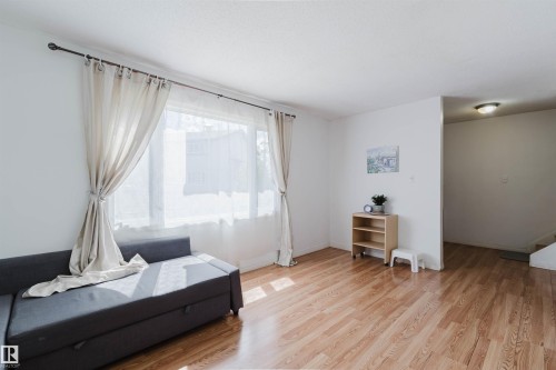Spacious living area featuring expansive windows with drapery, wood-finish flooring, and crisp white walls - 4 14310 80 Street, Edmonton, AB 