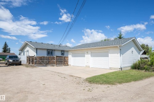 Two-car attached garage with concrete driveway, light blue siding, and a wooden fence - 10232 101 Street, Westlock, AB 