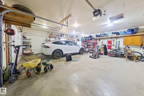 Spacious garage with a concrete floor, overhead storage shelving, mounted wall shelving, recessed lighting, and a white garage door - 10232 101 Street, Westlock, AB 