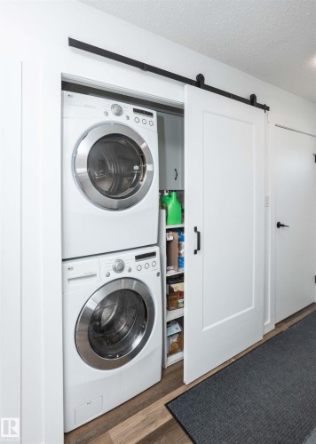 Dedicated laundry area featuring a stacked washer and dryer, wood-finish flooring, and a barn door with matte black hardware - 10232 101 Street, Westlock, AB 