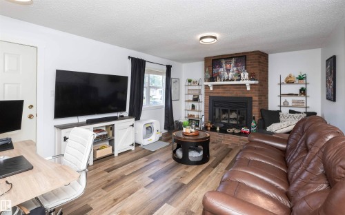 Living area featuring wood-finish flooring, a brick-surround fireplace with a white mantel, and built-in shelving - 10232 101 Street, Westlock, AB 