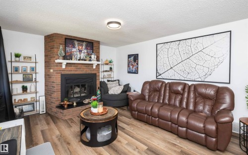 Living space featuring wood-finish flooring, a brick fireplace with a black firebox, a white mantel, and ceiling-mounted lighting - 10232 101 Street, Westlock, AB 