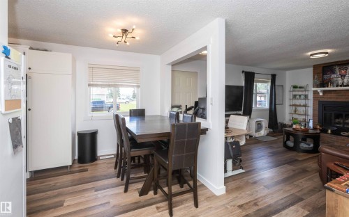 Open-concept living space featuring wood-finish flooring, a dining area with a modern light fixture, and a brick fireplace with a mantle - 10232 101 Street, Westlock, AB 