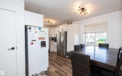 Kitchen and dining area featuring wood-finish flooring, white cabinetry with dark hardware, a large window, and modern ceiling light fixtures - 
