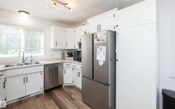 Kitchen featuring wood-finish flooring, white cabinetry with black hardware, stainless steel appliances, and a double basin sink - 