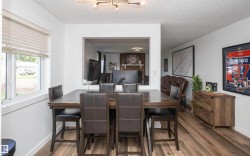Open-concept dining area featuring wood-finish flooring, a contemporary ceiling light fixture, and white painted walls - 