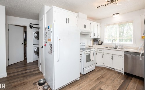 Kitchen with white cabinetry, wood-finish flooring, stainless steel dishwasher, and stacked laundry appliances - 10232 101 Street, Westlock, AB 