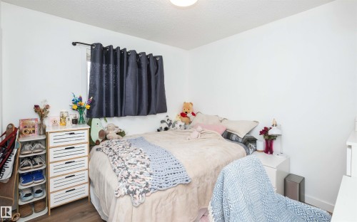 Bright interior room featuring white walls, a single window with dark curtains, wood-finish flooring, and a ceiling-mounted light fixture - 10232 101 Street, Westlock, AB 