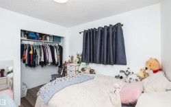 Bedroom featuring wood-finish flooring, a built-in closet with shelving and hanging space, white walls, a mounted light fixture, and a window with dark curtains - 