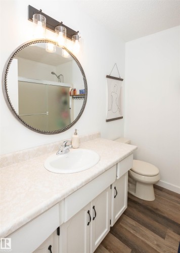 Bathroom vanity featuring a white oval sink set into a cream-toned countertop, white cabinetry with black hardware, and wood-finish flooring - 10232 101 Street, Westlock, AB 