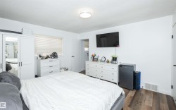 Bedroom featuring wood-finish flooring, a contemporary flush-mount ceiling light, white walls, a window with horizontal blinds, and a mounted television - 
