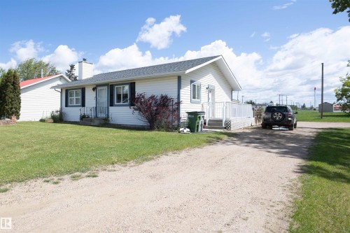 Single-story residence featuring white siding, a dark shingle roof, and a gravel driveway - 10232 101 Street, Westlock, AB 
