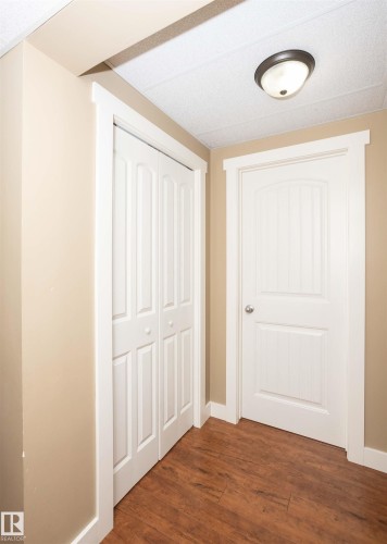 Warm beige walls with white trim, wood-finish flooring, white bifold closet doors, and a flush mount ceiling light - 10232 101 Street, Westlock, AB 