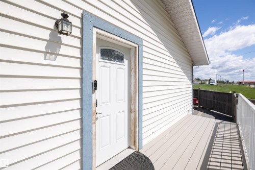 Exterior entry featuring a white paneled door with an arched glass insert, blue trim, white horizontal siding, a classic outdoor lantern, and a composite deck with white railings - 10232 101 Street, Westlock, AB 