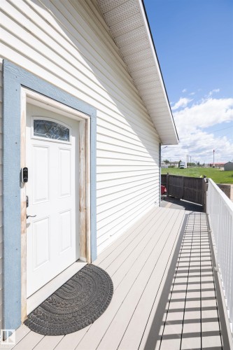 Front entry featuring a white panel door with leaded glass insert, blue trim, white vinyl siding, and a light-toned composite deck extending to a white railing - 10232 101 Street, Westlock, AB 