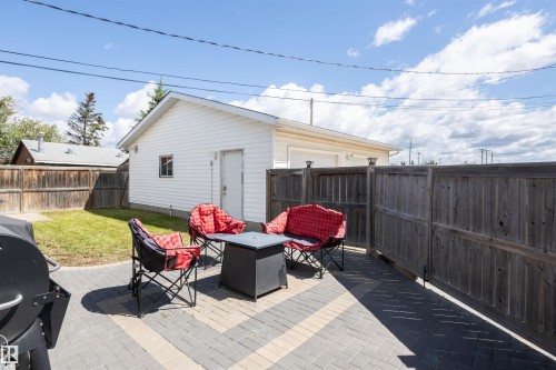 Expansive backyard featuring a paver patio with a herringbone pattern, a detached garage with white siding, a wooden privacy fence, and a grassy lawn area - 10232 101 Street, Westlock, AB 