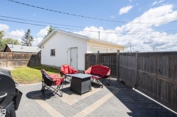 Expansive backyard featuring a paver patio with a herringbone pattern, a detached garage with white siding, a wooden privacy fence, and a grassy lawn area - 