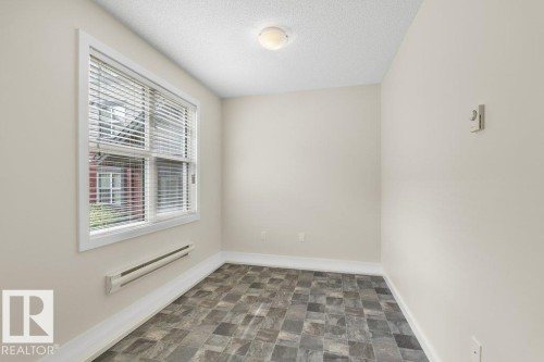 Bright room featuring a prominent window with white blinds, textured ceiling, flush mount lighting, patterned tile-finish flooring, and white baseboards - 125 655 Watt Boulevard, Edmonton, AB 