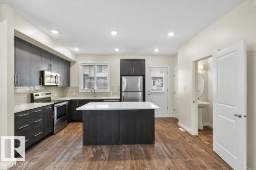 Kitchen featuring wood-finish flooring, dark wood-finish cabinetry, a white countertop island, stainless steel appliances, and recessed lighting - 125 655 Watt Boulevard, Edmonton, AB 
