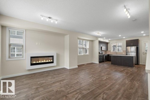Open-concept living space featuring wood-finish flooring, a wall-mounted electric fireplace, recessed lighting, and track lighting - 125 655 Watt Boulevard, Edmonton, AB 