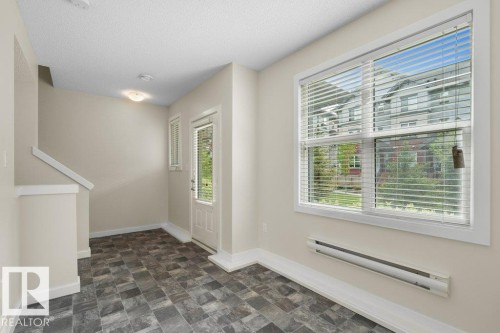 Entryway featuring patterned tile flooring, a half-glass entry door with vertical blinds, a large window with horizontal blinds, and baseboard heating - 125 655 Watt Boulevard, Edmonton, AB 