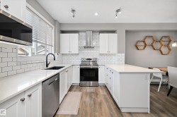 U-shaped kitchen featuring white cabinetry, light-colored countertops, stainless steel appliances, and a subway tile backsplash - 