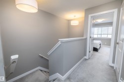Carpeted hallway and staircase featuring light gray walls, white trim, contemporary drum pendant lighting, and a white interior door leading to a room with a large window - 