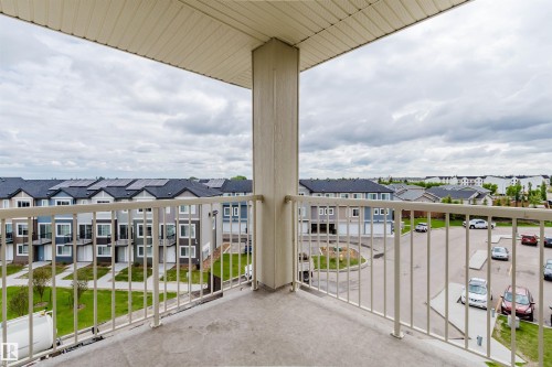 Concrete balcony with cream-colored metal railing, overlooking a residential area with varied housing styles and community green spaces - 402 3670 139 Avenue, Edmonton, AB 