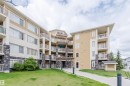 Multi-story building exterior featuring light-colored siding, stone accents, multiple balconies with metal railings, and a ground-level lawn area - 402 3670 139 Avenue, Edmonton, AB 