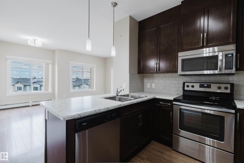 Contemporary kitchen featuring dark wood cabinetry, stainless steel appliances, a subway tile backsplash, and light-toned countertops - 402 3670 139 Avenue, Edmonton, AB 
