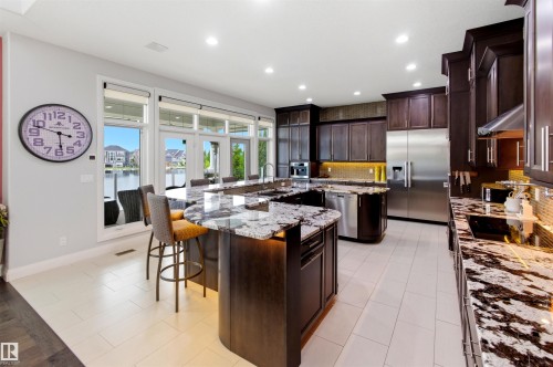 Kitchen featuring a large waterfall island with seating, dark wood-finish cabinetry, stainless steel appliances, and light tile flooring - 9003 16 Avenue, Edmonton, AB 