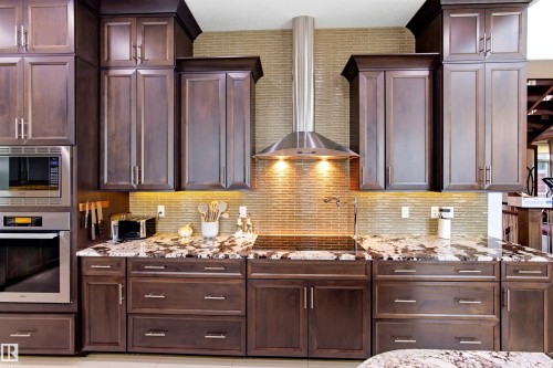 Kitchen featuring dark wood cabinetry, stainless steel appliances, and a mosaic tile backsplash - 9003 16 Avenue, Edmonton, AB 