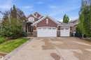 Stucco and stone facade home featuring a multi-car driveway, arched entryway, and dual white garage doors with window inserts - 9003 16 Avenue, Edmonton, AB 
