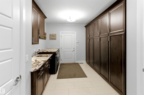 Utility room featuring extensive dark wood cabinetry, light-toned tile flooring, and a countertop with integrated sink - 9003 16 Avenue, Edmonton, AB 