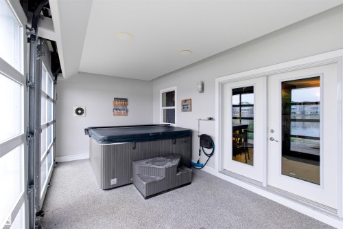 Covered patio with a spa, offering a lake backdrop through glass panel doors - 9003 16 Avenue, Edmonton, AB 