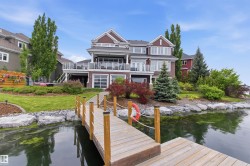 Waterfront property featuring a private wooden dock, manicured landscaping, and a multi-level deck with glass railings - 