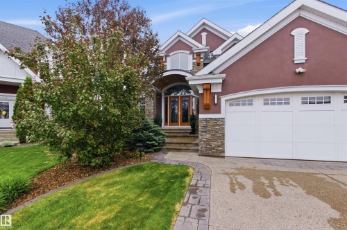 Two-car garage with frosted window panels, stone veneer accents, stucco exterior, arched double-door entry, and a paver walkway - 9003 16 Avenue, Edmonton, AB 