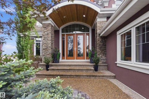 Grand arched entry with wood-paneled ceiling, double wood doors with glass inserts, stacked stone columns, and complementary stucco siding - 9003 16 Avenue, Edmonton, AB 