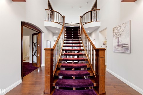 Grand two-story foyer featuring a curved staircase with a wood handrail, metal balusters, and carpeted treads - 9003 16 Avenue, Edmonton, AB 