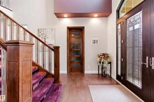 Foyer featuring hardwood flooring, a grand staircase with wood newel posts and metal balusters, and a rich wood entry door with decorative glass inserts - 9003 16 Avenue, Edmonton, AB 