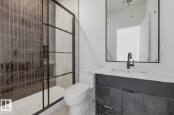 Bathroom featuring a walk-in shower with dark-toned vertical tile and a black-framed glass enclosure - 